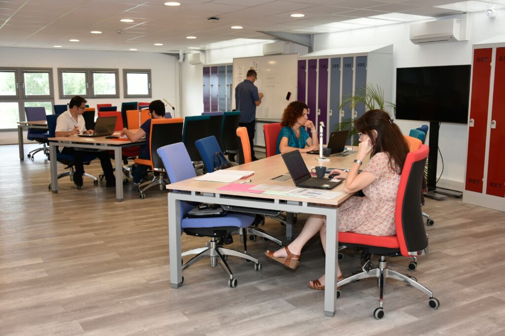 Salle de coworking ou plusieurs personnes travaillent. Un espace très colorés avec différentes couleurs pour chaque chaises (bleu, rouge, vert)