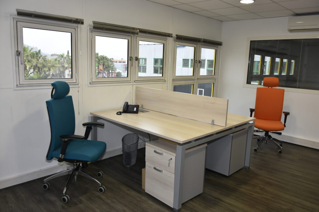 Un bureaux en bois clairs avec deux chaises de couleurs, l'une est bleu, l'autre est orange